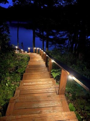 Un chemin en bois, bordé de rampes et illuminé de guirlandes lumineuses, mène à un bâtiment.