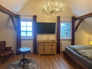 A bedroom with a wooden ceiling, a chandelier, a TV, a bed, a dresser, a chair, and two windows with curtains. - Bergfreiheit 61 (Winterberg)