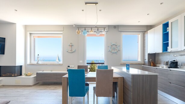 A modern kitchen with a central island, large windows with ocean views, and nautical decor. - Wanderlust by Monholiday (Monopoli)