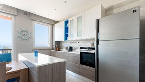 A modern kitchen with a stainless steel refrigerator, wooden cabinets, and a view of the sea. - Wanderlust by Monholiday (Monopoli)
