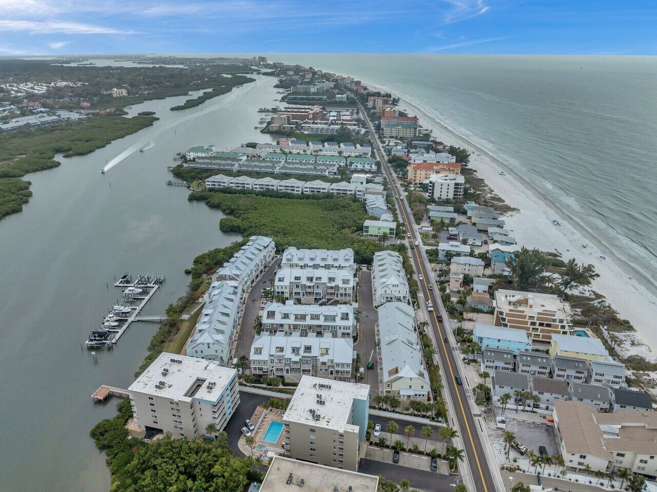 An aerial view of a coastal residential area with a marina, beachfront properties, and a river running parallel to the beach.