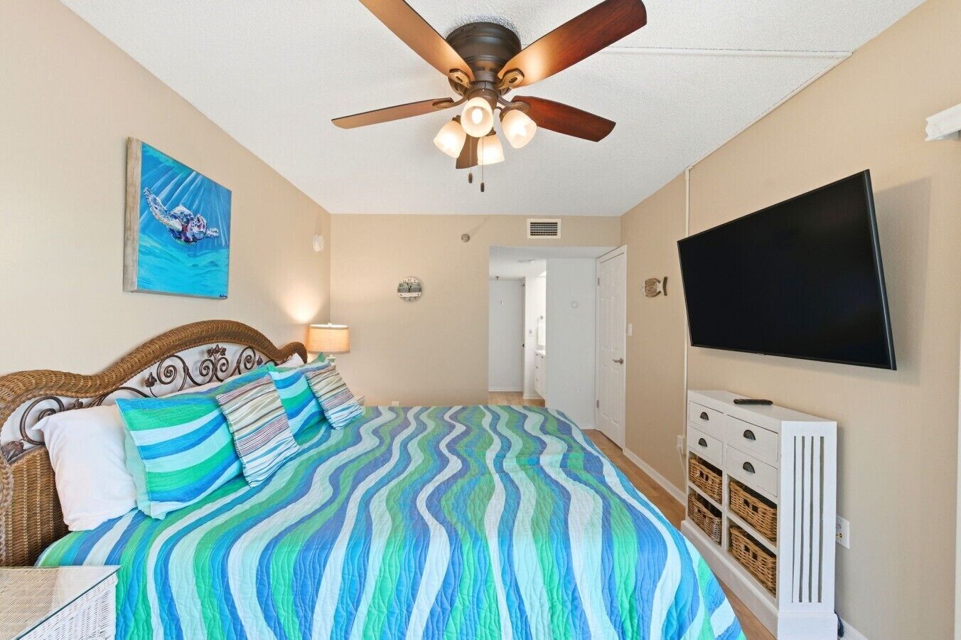 Una camera da letto con un letto, una ventola a soffitto, una TV e un quadro appeso al muro.