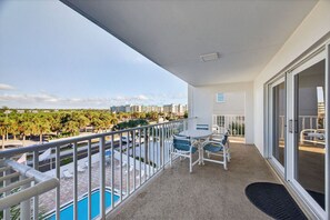 Balcón con vista a la piscina, barandilla blanca y una mesa con sillas.