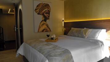 Ein Hotelzimmer mit einem großen Bett, einem hölzernen Kopfteil, einem Wandbild und einer Ablage mit Wein und Blumen.