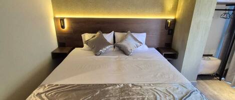 A modern bedroom with a large bed, built-in nightstands, and a headboard with integrated lighting.