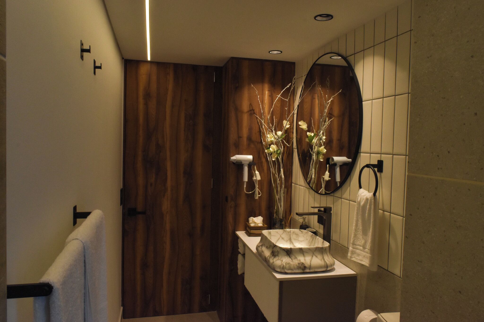 A modern bathroom with a wooden accent wall, a marble sink, and a mirror with a towel hanging on the wall.