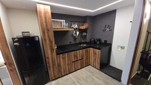 A modern kitchen with a black refrigerator, wooden cabinets, a black countertop, and a built-in sink. - Mali Experience (Rionegro)