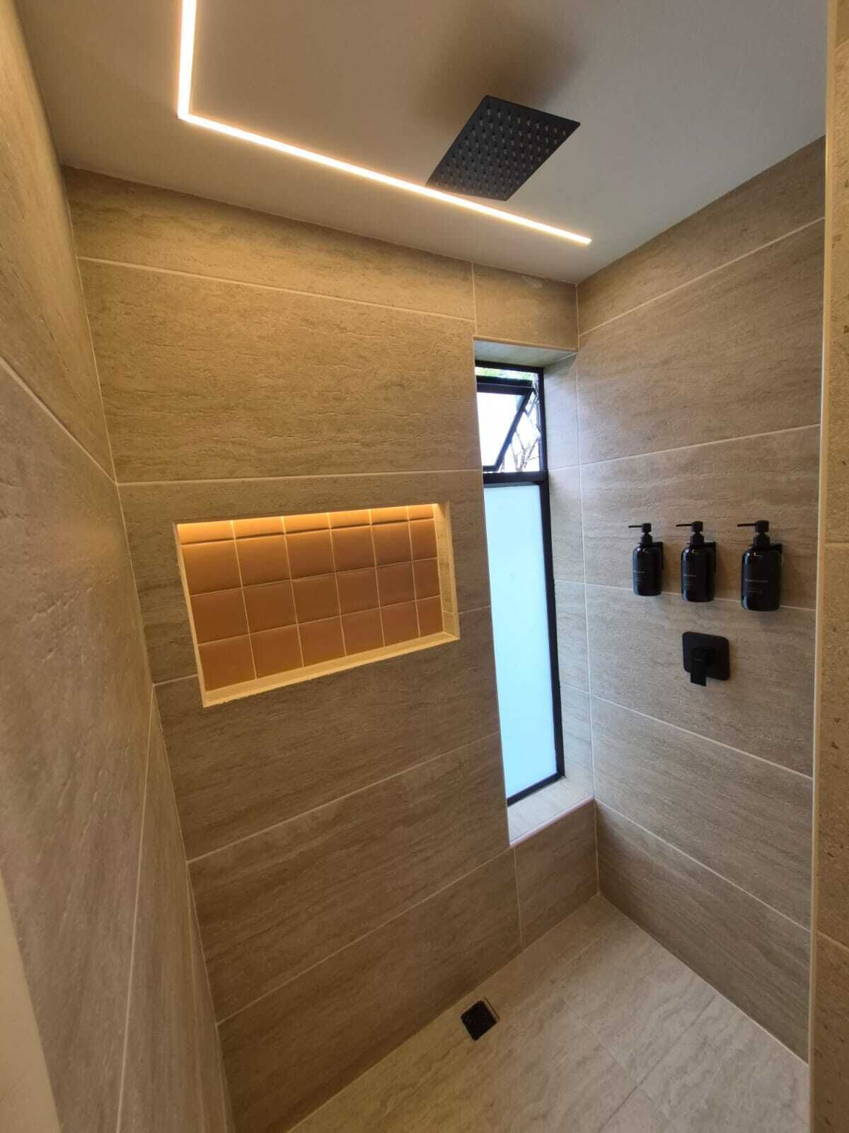 A modern bathroom with a shower area, a window, and three black dispensers on the wall.