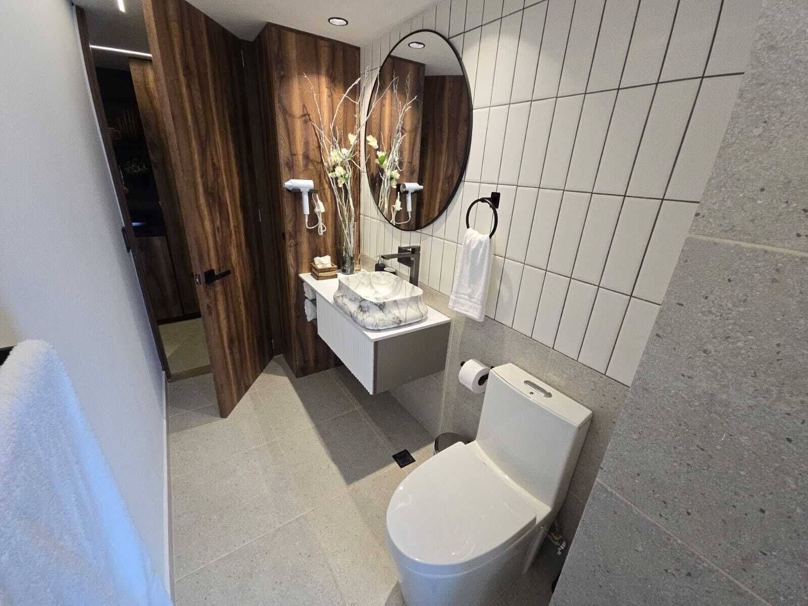 Un baño moderno con tocador de madera, lavamanos de mármol, inodoro y espejo.