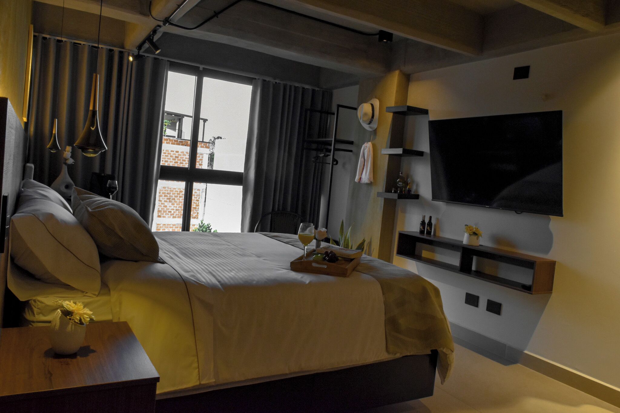 A modern hotel room with a large bed, a flat-screen TV, a wooden side table, and a view of the outside.