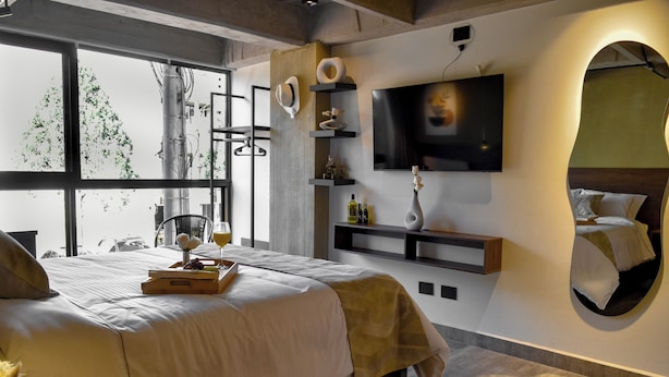 A modern hotel room with a large bed, a TV mounted on the wall, and a view of the outdoors through large windows. - Mali Experience (Rionegro)
