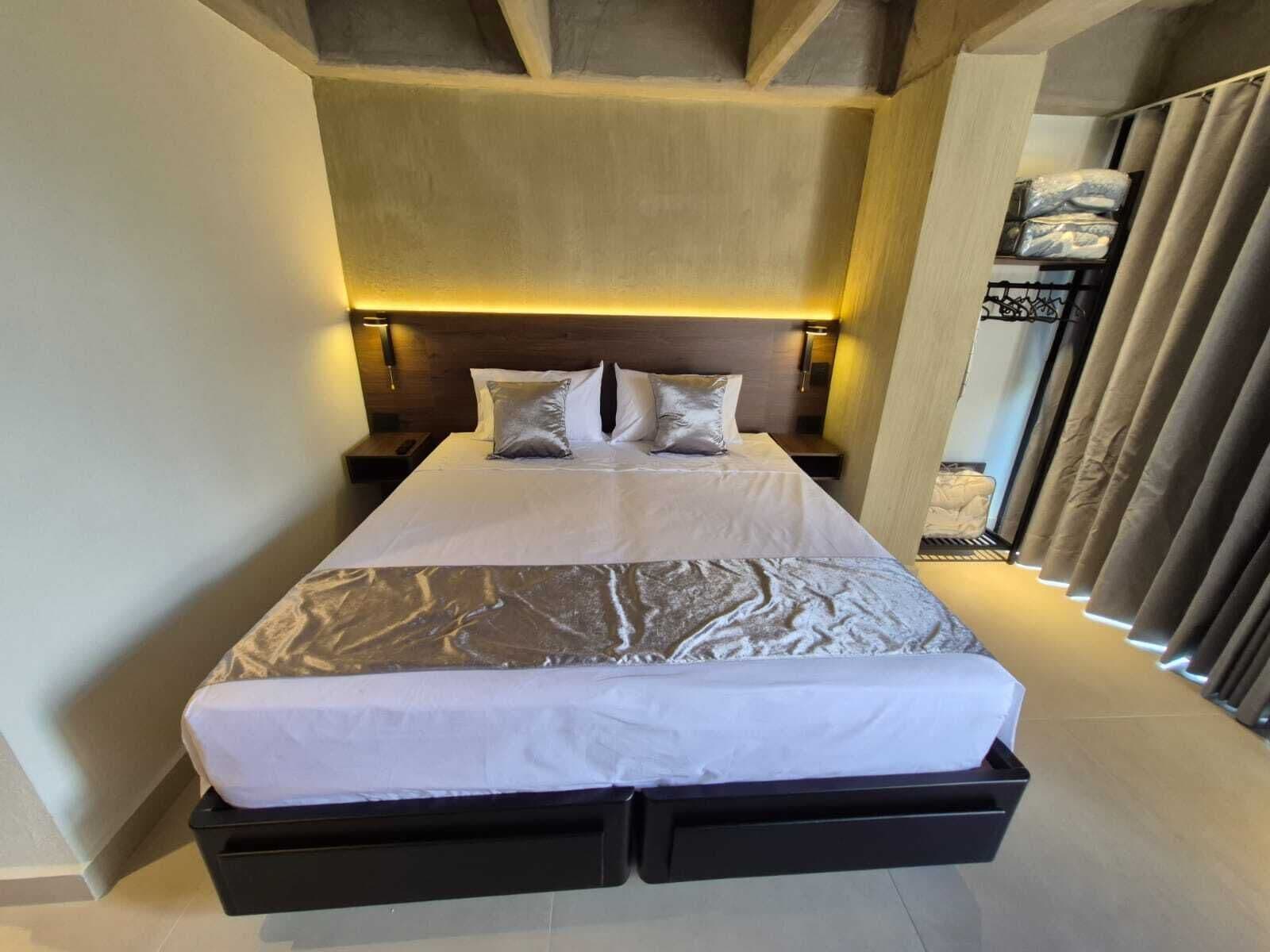 A modern hotel room with a large bed, bedside tables, and a headboard with integrated lighting.