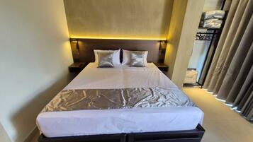A modern hotel room with a large bed, bedside tables, and a headboard with integrated lighting.