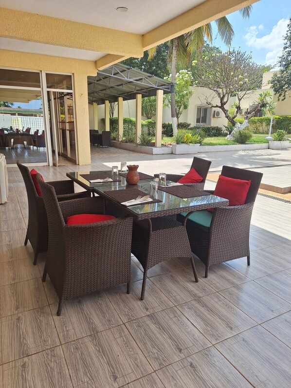 An outdoor seating area with wicker furniture and a glass table. - Hôtel Les Frontières Odienné (Odienné)