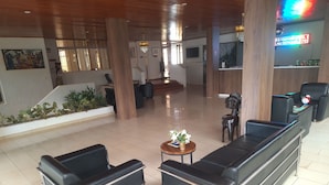 A lobby with a reception desk, black leather sofas, a small round table with flowers, and a staircase in the background. - Hôtel Les Frontières Odienné (Odienné)