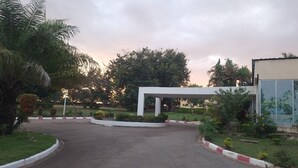 A paved entrance with a white canopy structure, surrounded by greenery and a clear sky. - Hôtel Les Frontières Odienné (Odienné)