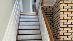 A staircase with white balustrades and black steps, leading to a room with a brick wall. - Dean's Seaside Escape,
Beautiful beaches and awesome sunrise and sunsets! (Cape Tormentine)