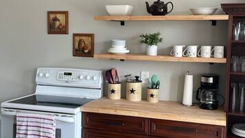 Eine Küche mit Herd, Backofen, Holzschränken und Regalen mit Geschirr und Besteck.