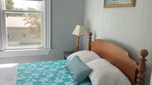 A bedroom with a bed, a window, a lamp, and a painting on the wall.