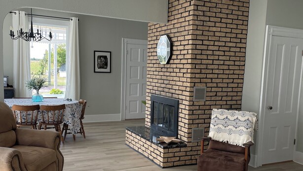 A living room with a brick fireplace, a dining area with a table and chairs, and a cozy seating area with a chair and ottoman. - Dean's Seaside Escape,
Beautiful beaches and awesome sunrise and sunsets! (Cape Tormentine)