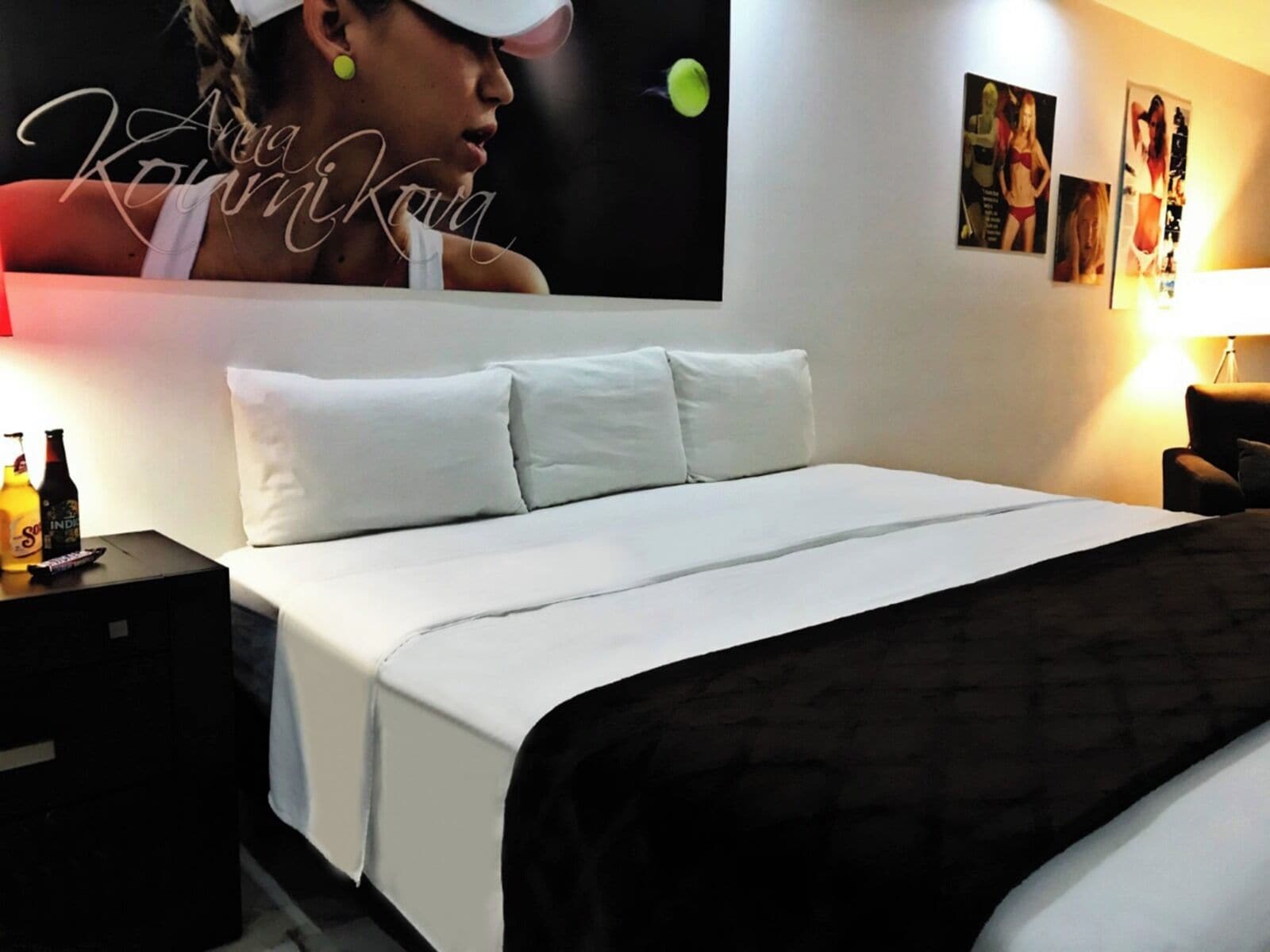 A hotel room with a large bed, white bedding, a nightstand with a remote control, and a poster on the wall.