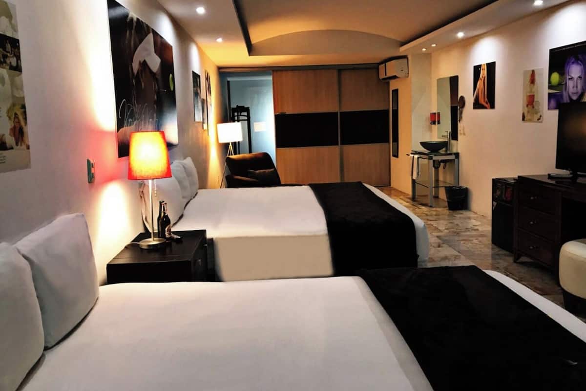 A hotel room with two beds, a desk, a chair, a TV, and a minibar.