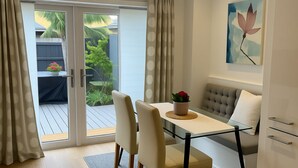 A modern dining area with a glass table, four chairs, and a sofa. There is a sliding glass door leading to a balcony with plants. - London 3 Bedroom Home - Private Garden, Free Parking, Near Tower of London! (London)