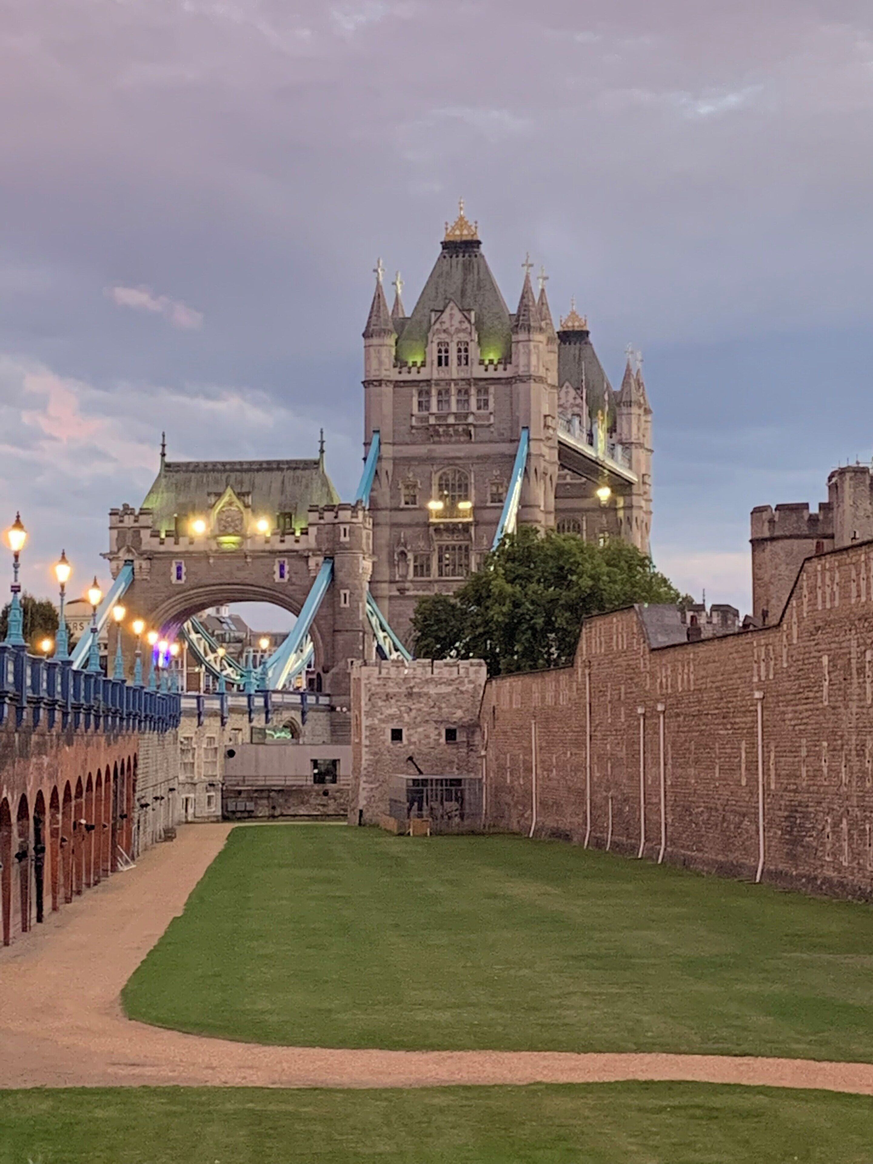 A historic castle with a large arch bridge, a well-maintained lawn, and a stone wall.