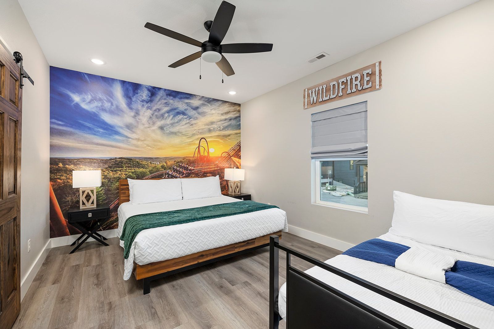 Ein Schlafzimmer mit Bett, Deckenventilator, Nachttisch, Lampe, Fenster mit Blick und Wandgemälde.
