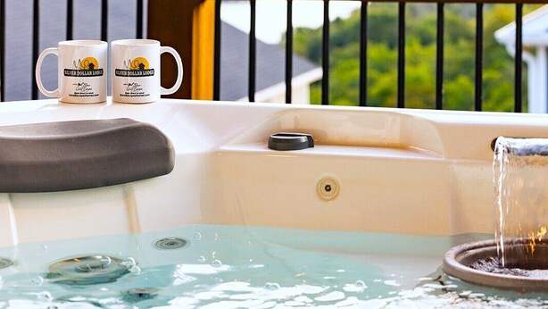 Un bain à remous avec vue sur un plan d’eau et des collines, deux tasses sur une table et une rambarde.