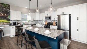 Une cuisine moderne avec des armoires blanches, un comptoir en granit, des appareils électroménagers en acier inoxydable et des luminaires suspendus.