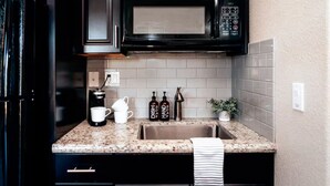A kitchen with a stainless steel sink, a coffee maker, two bottles of dish soap, and a potted plant.