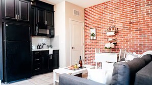 A modern kitchen with black cabinets, a white countertop, and a brick wall.