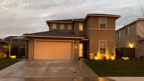 A modern two-story house with a garage, well-maintained lawn, and exterior lighting.