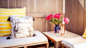 A cozy outdoor seating area with a wooden bench and a table, featuring a vase with flowers and glasses.