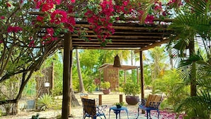 A covered outdoor seating area with a pergola, surrounded by lush greenery and flowering plants. - Recanto Verde (Mata de Sao Joao)