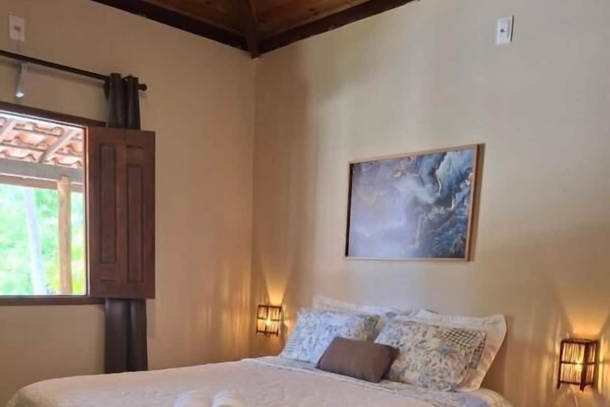 A neatly made bed with a white duvet, two rolled towels, and a blue striped rug on a tiled floor.