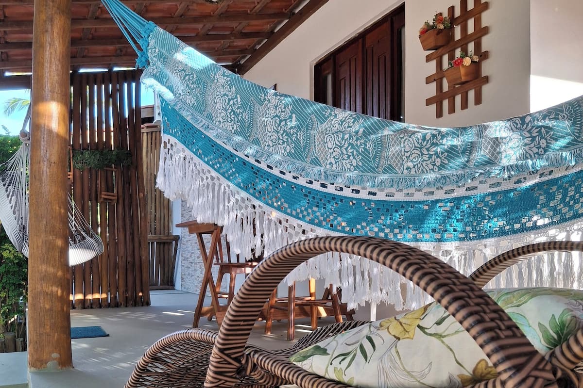 A hammock chair with a floral cushion, a wooden table, and a wall with a wooden cross symbol.