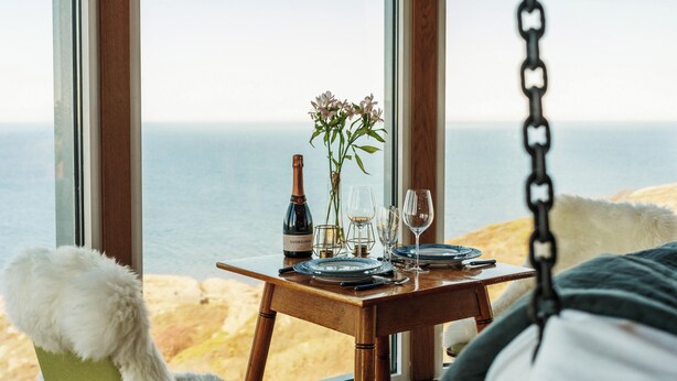 A dining area with a table set for two, overlooking a beach. - Falknästet unique accommodation in one of Sweden's most spectacular natural areas. (Höganäs)