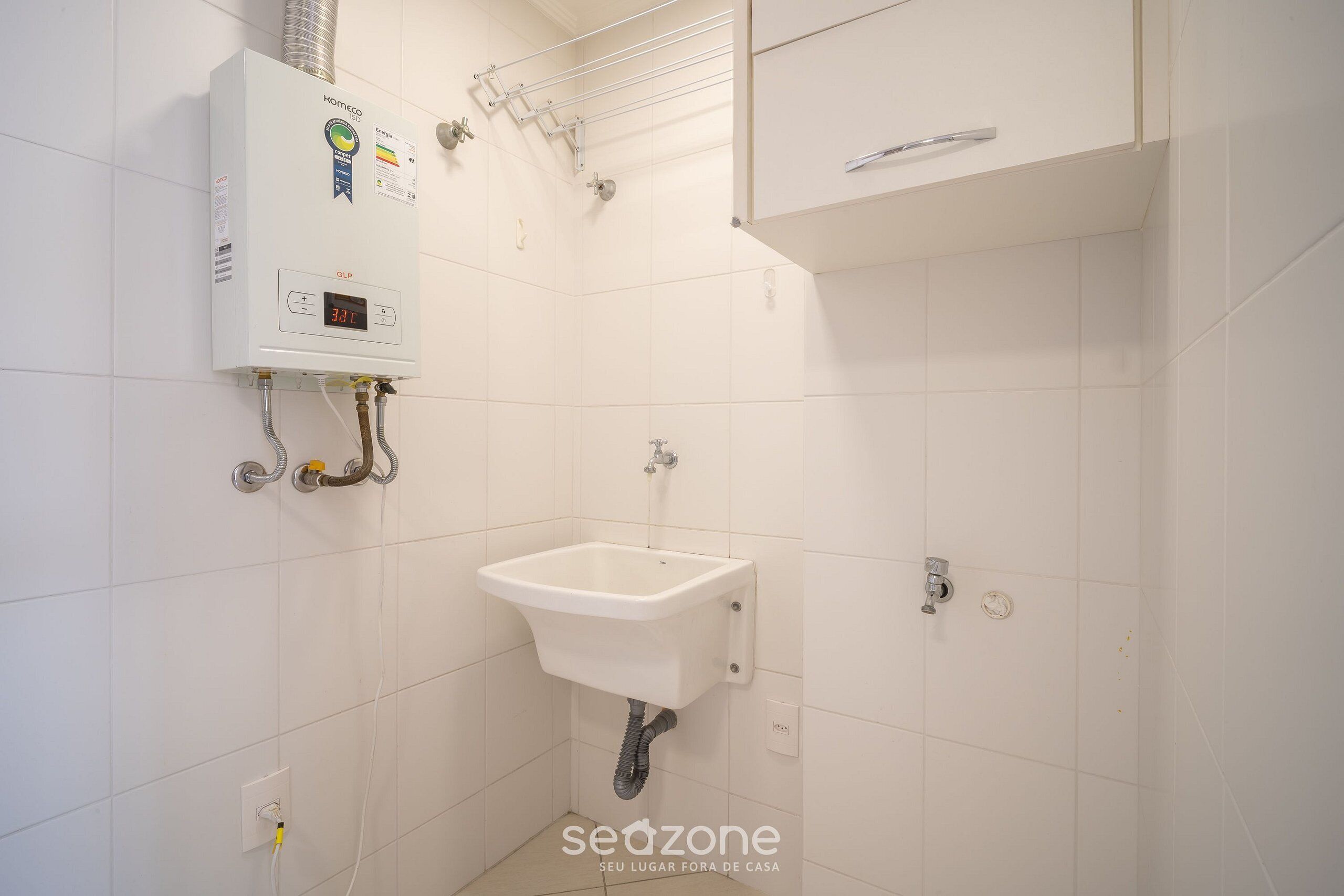 Une salle de bain avec un mur recouvert de carreaux blancs, un lavabo encastré, des toilettes et un chauffe-eau.