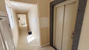 A hallway with a tiled floor, a door with a granite frame, and a fire alarm on the wall. - Apts in a Building 100 Meters From Ufsc - Eoss (Florianópolis)