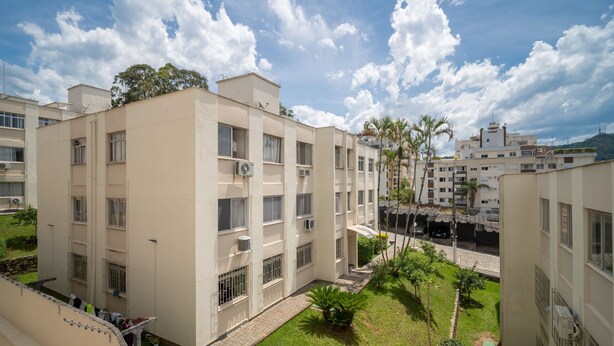 A multi-story residential building with balconies, air conditioning units, and a paved courtyard with small trees and shrubs. - Apts in a Building 100 Meters From Ufsc - Eoss (Florianópolis)