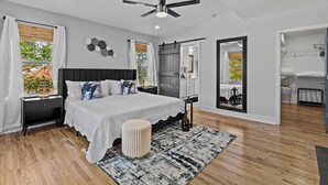 A modern bedroom with a large bed, a ceiling fan, and a view of the outdoors.