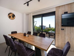 Une salle de réunion moderne, dotée d’une table en bois, de chaises sombres, d’une horloge représentant une carte du monde, de grandes fenêtres et d’un téléviseur fixé au mur.
