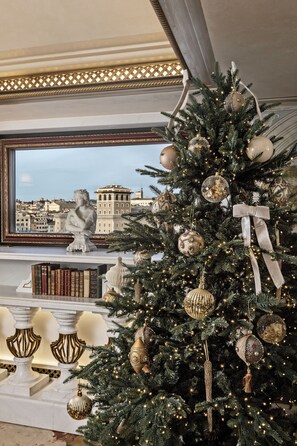 A Christmas tree with gold and white ornaments, positioned near a window overlooking a cityscape.