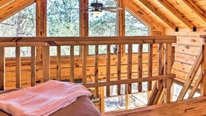 En træhytte med skråt tag, en balkon med gelænder og en loftsvifte.
