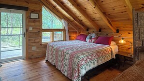 Et soveværelse i en træhytte med seng, vindue og loftslampe.