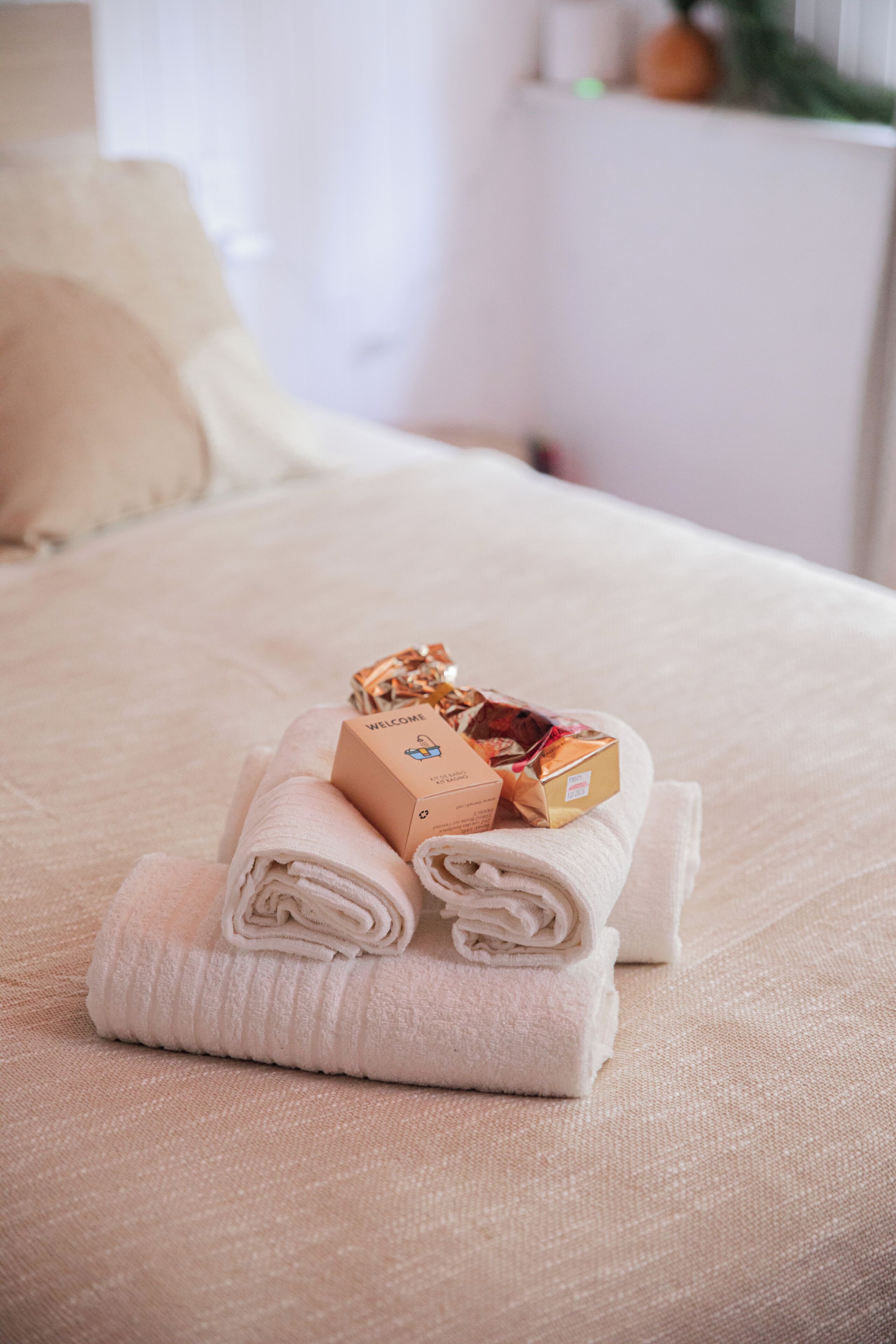 A neatly made bed with folded towels and a welcome box.