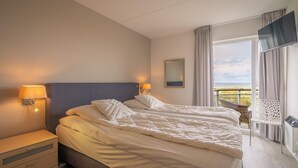 Ein Hotelzimmer mit einem großen Bett, zwei Nachttischlampen, einem Flachbildfernseher, einem Balkon mit Blick und einem Sessel.