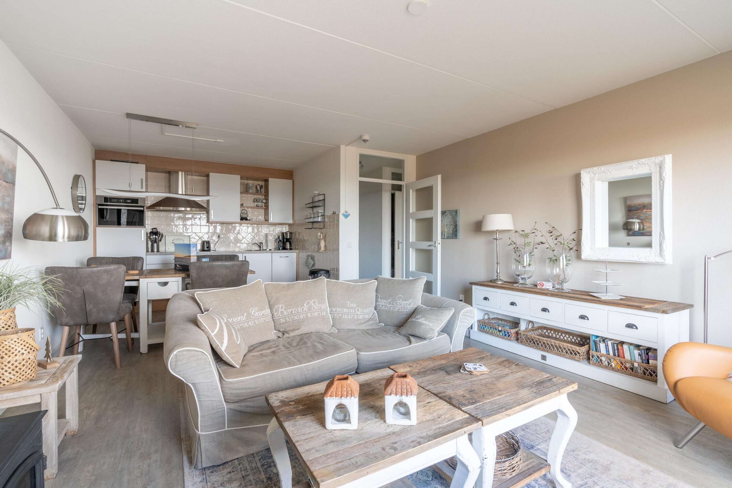 A modern living room with a grey sofa, wooden coffee table, and a kitchen in the background.